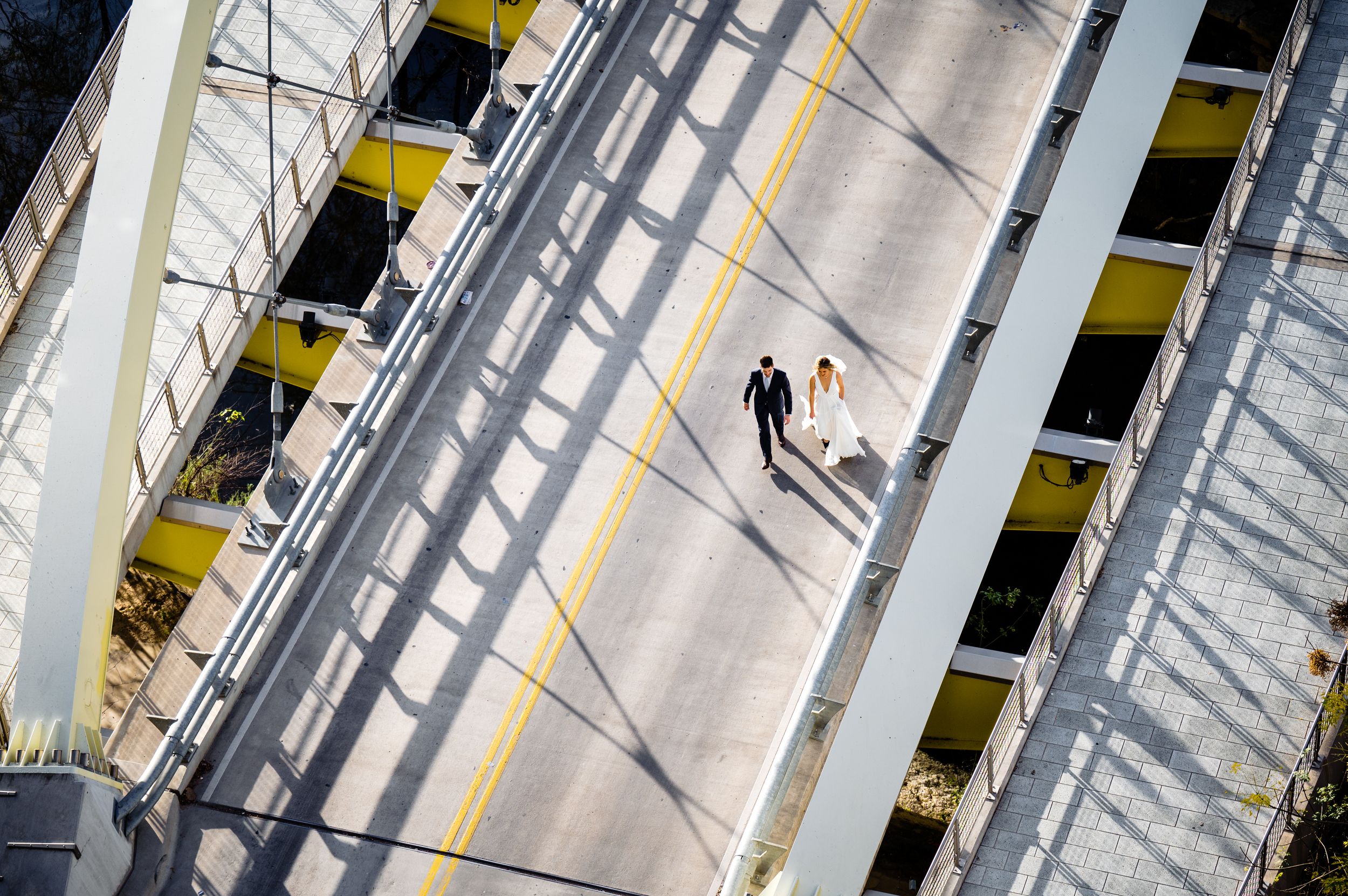 Aerial view of a lone figure walking on an empty street with dramatic diagonal shadows and yellow lines.