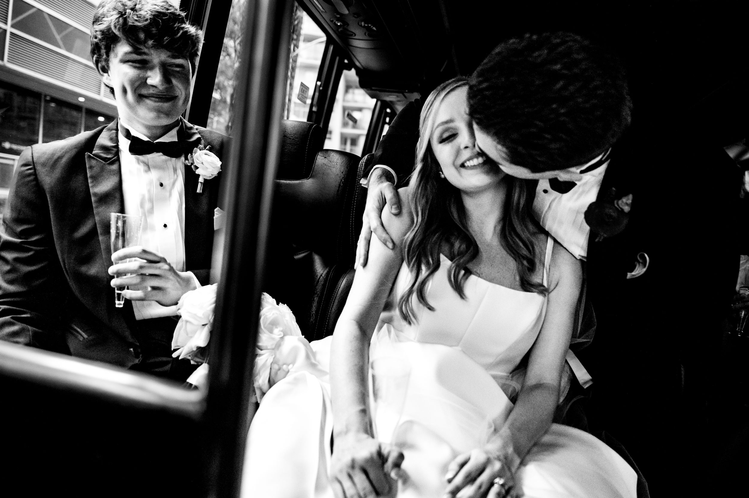 A black and white photo of a bride and groom sharing a joyful moment while riding public transportation.
