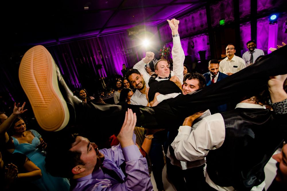 Crowd lifts and carries person horizontally during energetic dance party with purple lighting at night.