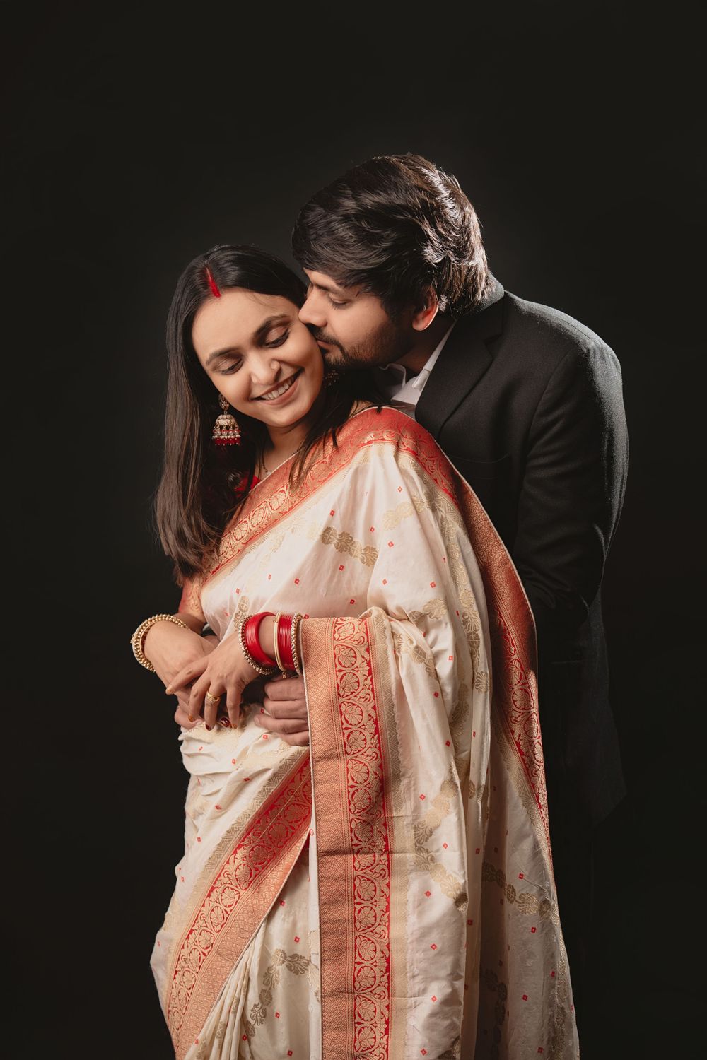 A romantic couple in traditional Indian attire sharing an intimate moment against a dark background.