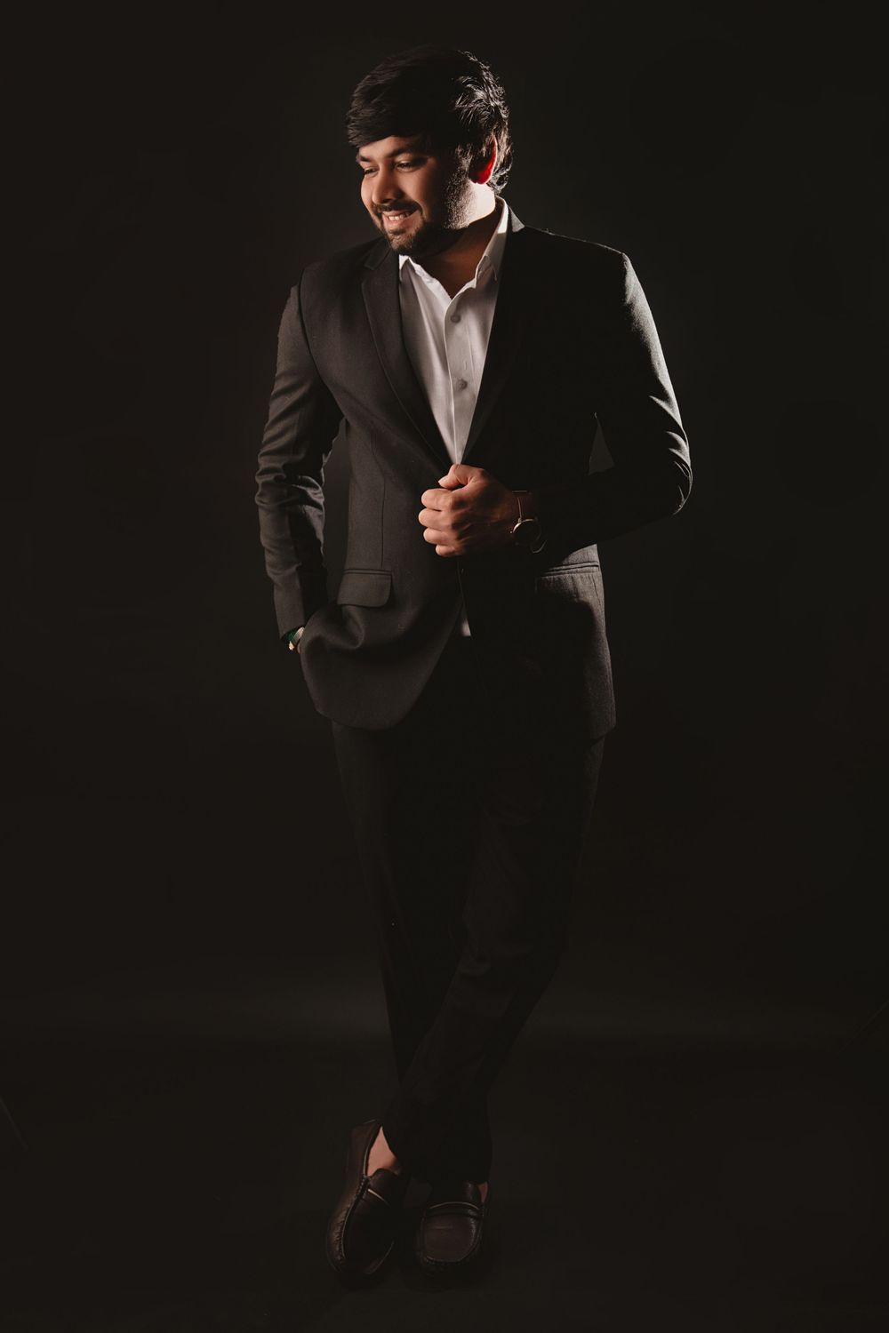 Man in dark suit poses dramatically against black background during creative photoshoot.