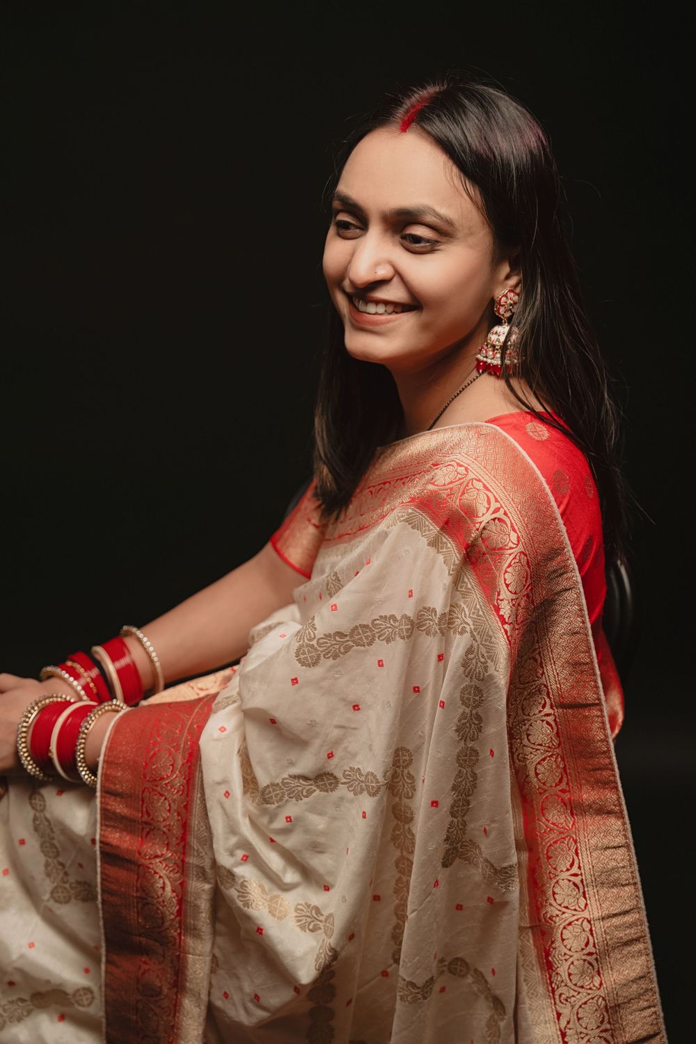 Person wearing cream and red traditional saree poses in profile against black background.