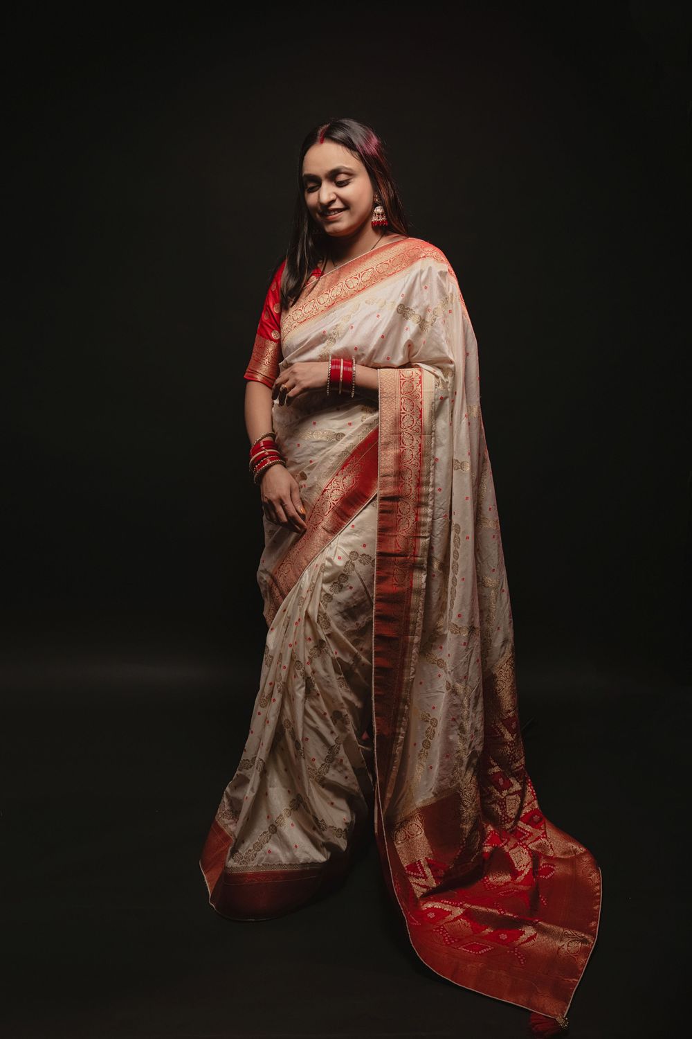 A glamorous photoshoot featuring someone in a beige and red silk saree striking elegant poses against a black backdrop.