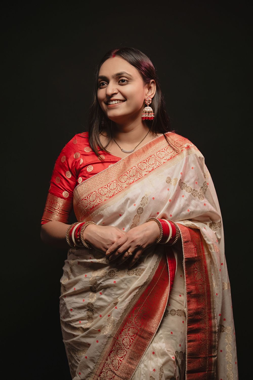 A person wears a traditional cream and red silk saree with ornate border details against a dark background.