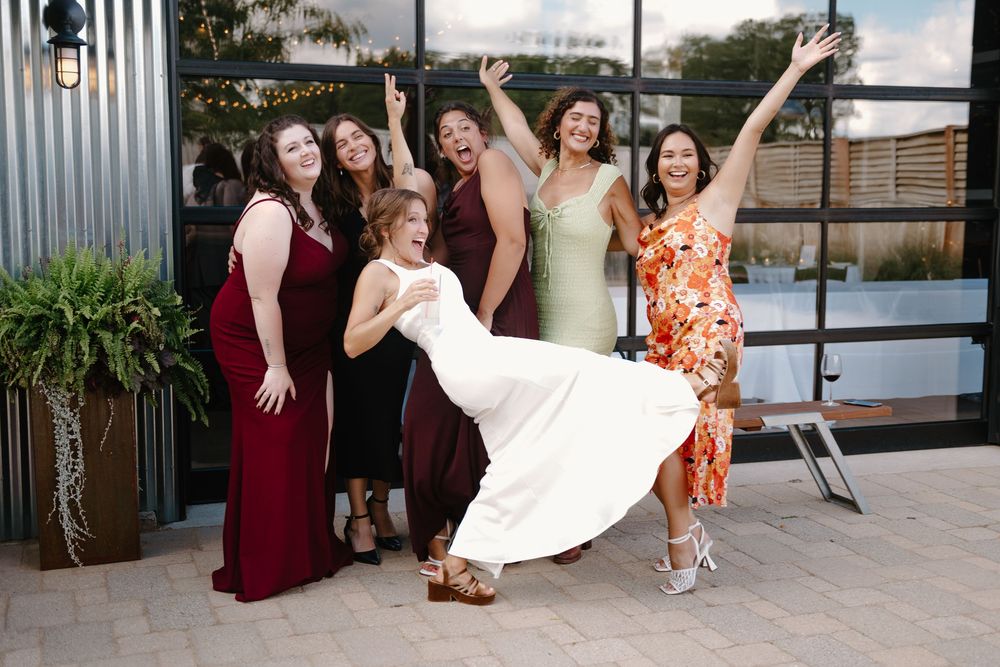 A group of wedding guests in burgundy and floral dresses dance together on an outdoor patio during a celebration.