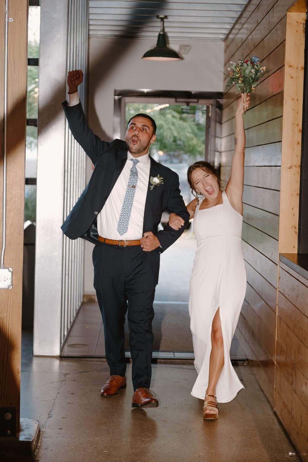 A joyful couple dancing and celebrating in a rustic wooden hallway with pendant lighting.