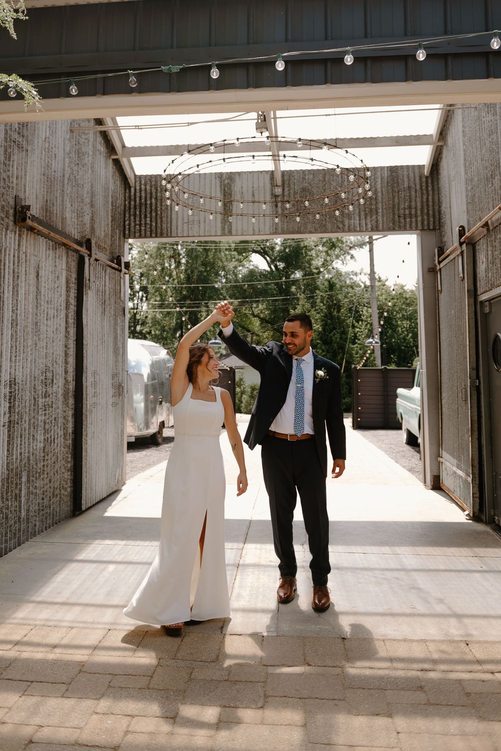A series of four wedding photos showing a couple walking and dancing together under a covered outdoor venue with string lights.
