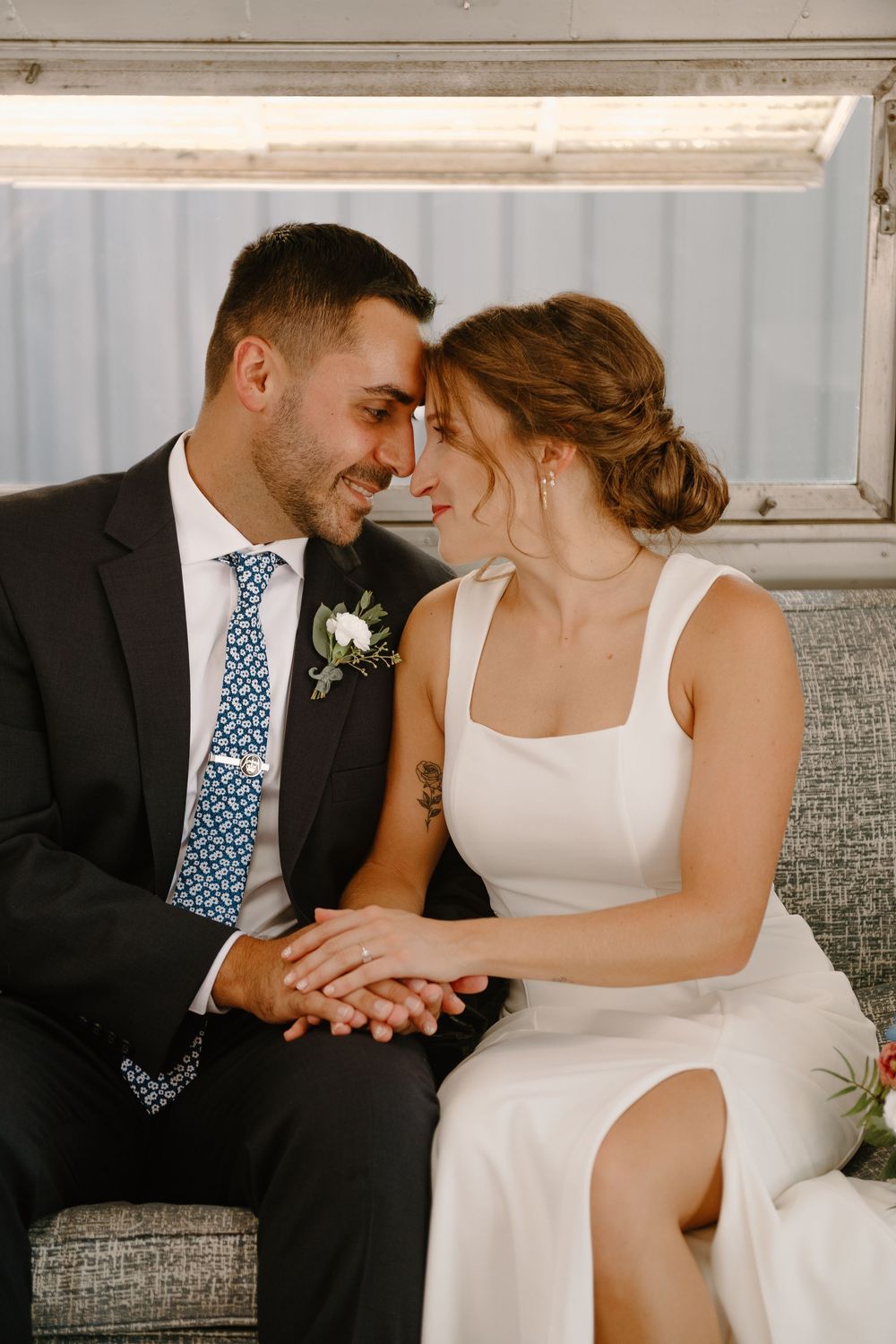 Romantic couple in wedding attire share intimate moments while sitting together on a gray couch in candid photo series.