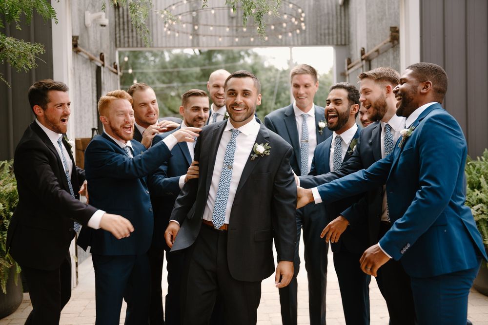 Groomsmen in navy suits share laughter and conversation during a wedding celebration.