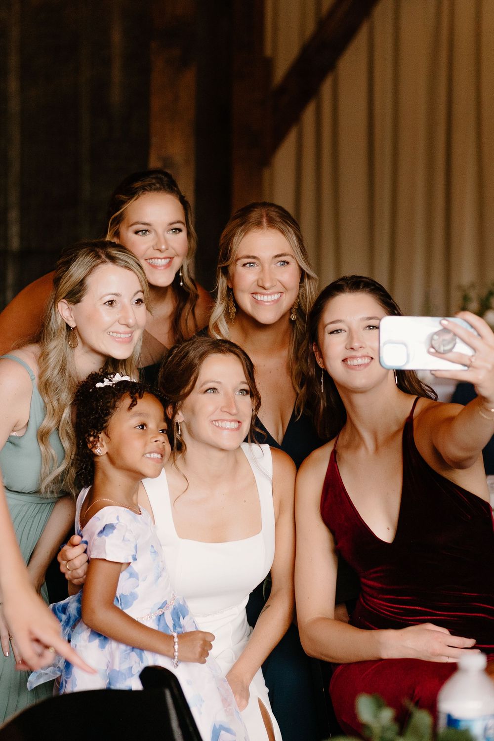 A group of friends in formal attire gather together to take a selfie at an indoor event.