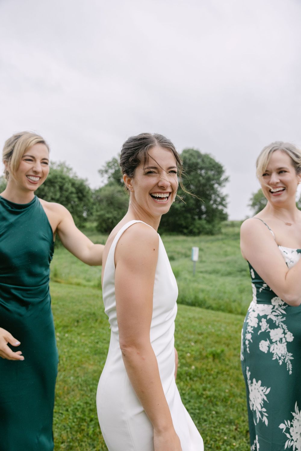 Three people in elegant dresses smile joyfully on a grassy lawn during what appears to be a special outdoor event.