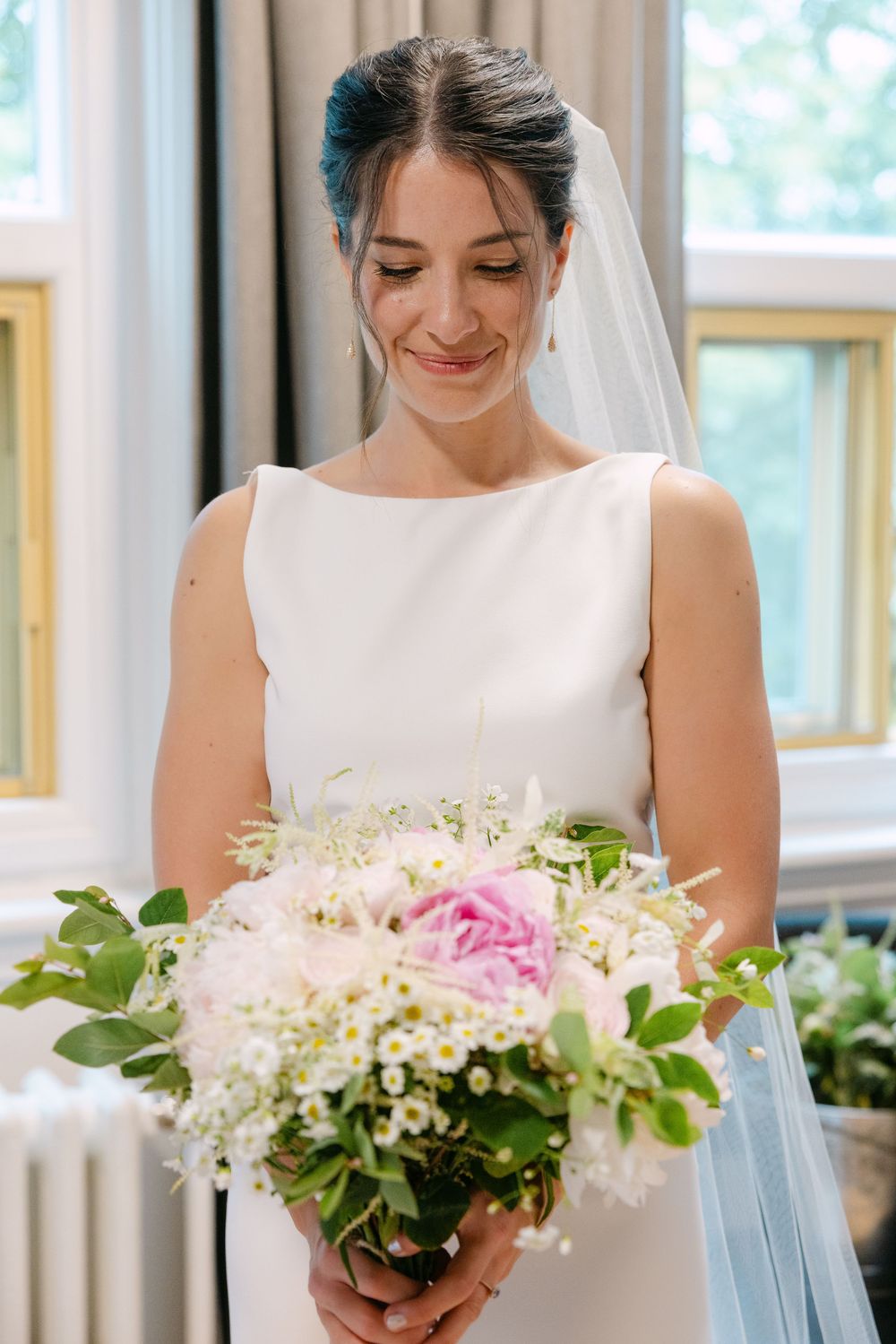 Bridesmaids in elegant white dresses holding pink and white floral bouquets stand together during a wedding ceremony.
