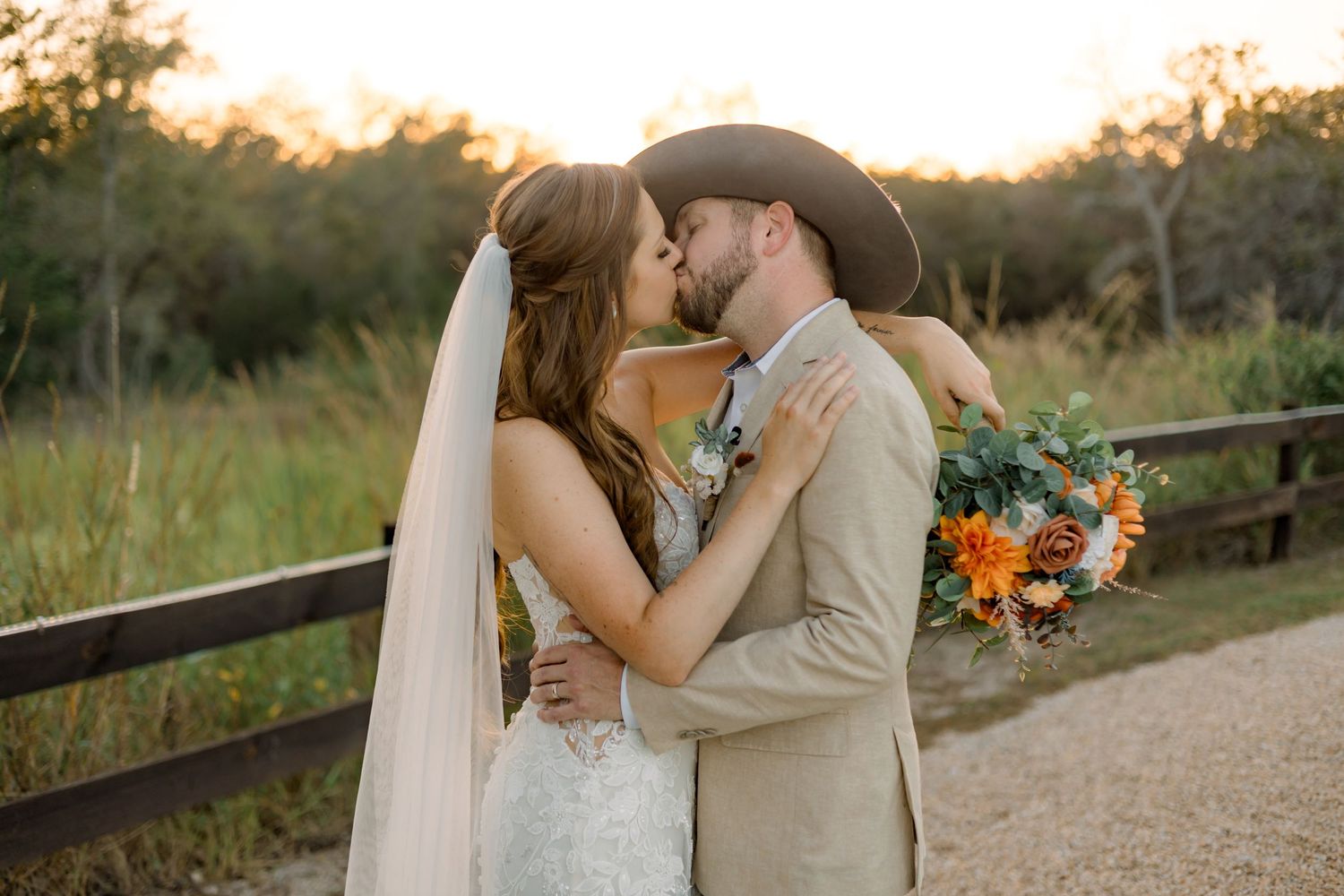 Sunset wedding portrait with couple embracing on a dirt path near wooden fence.