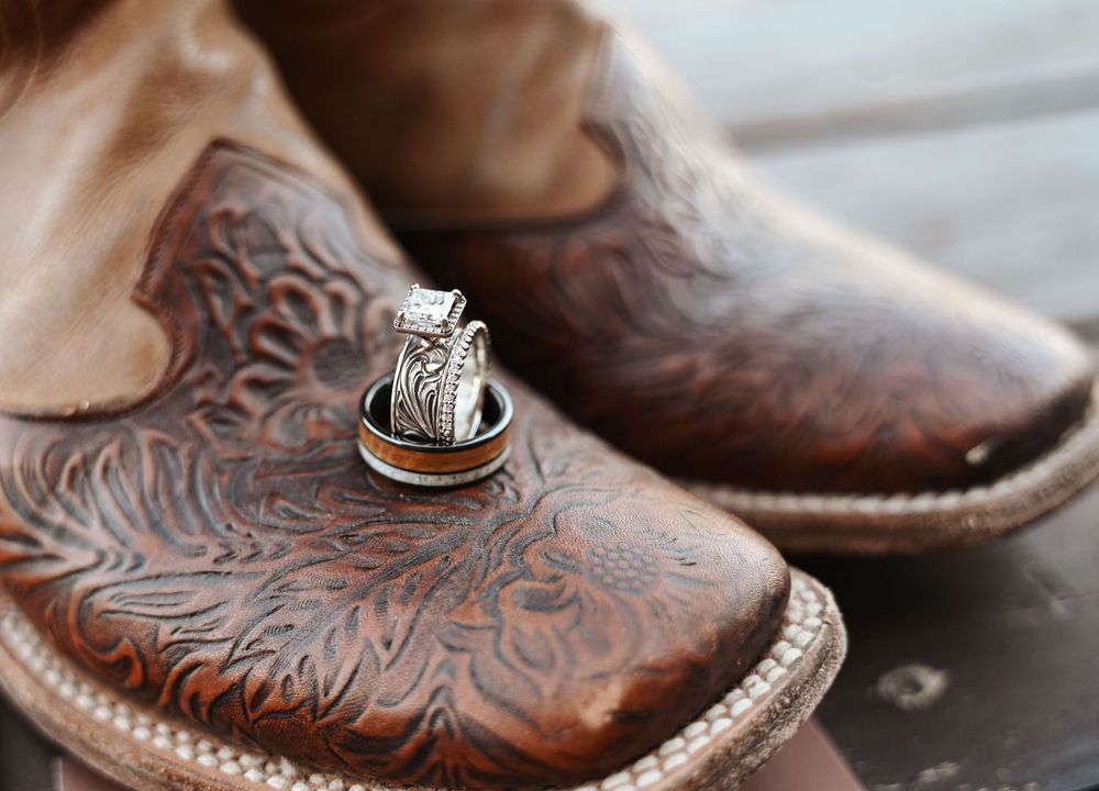 Wedding rings photographed on detailed brown leather cowboy boots.