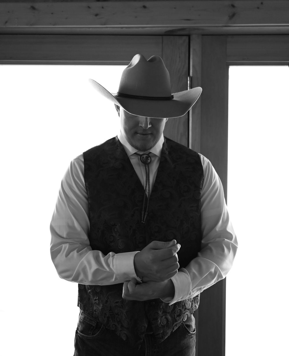 Silhouette of a person in western attire adjusting their tie in dramatic black and white lighting.