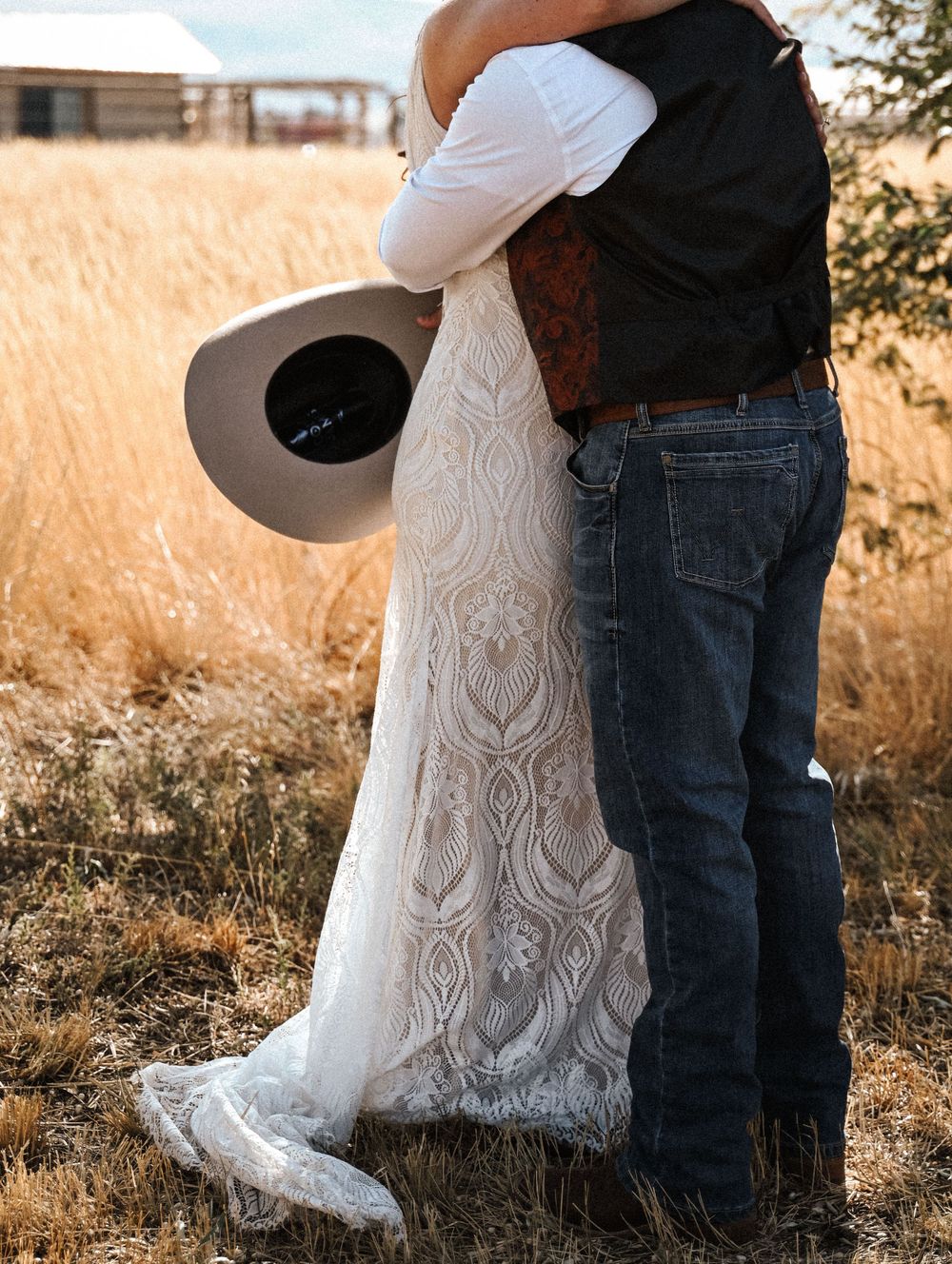A tender moment captured showing western attire and a white lace dress against golden wheat fields.