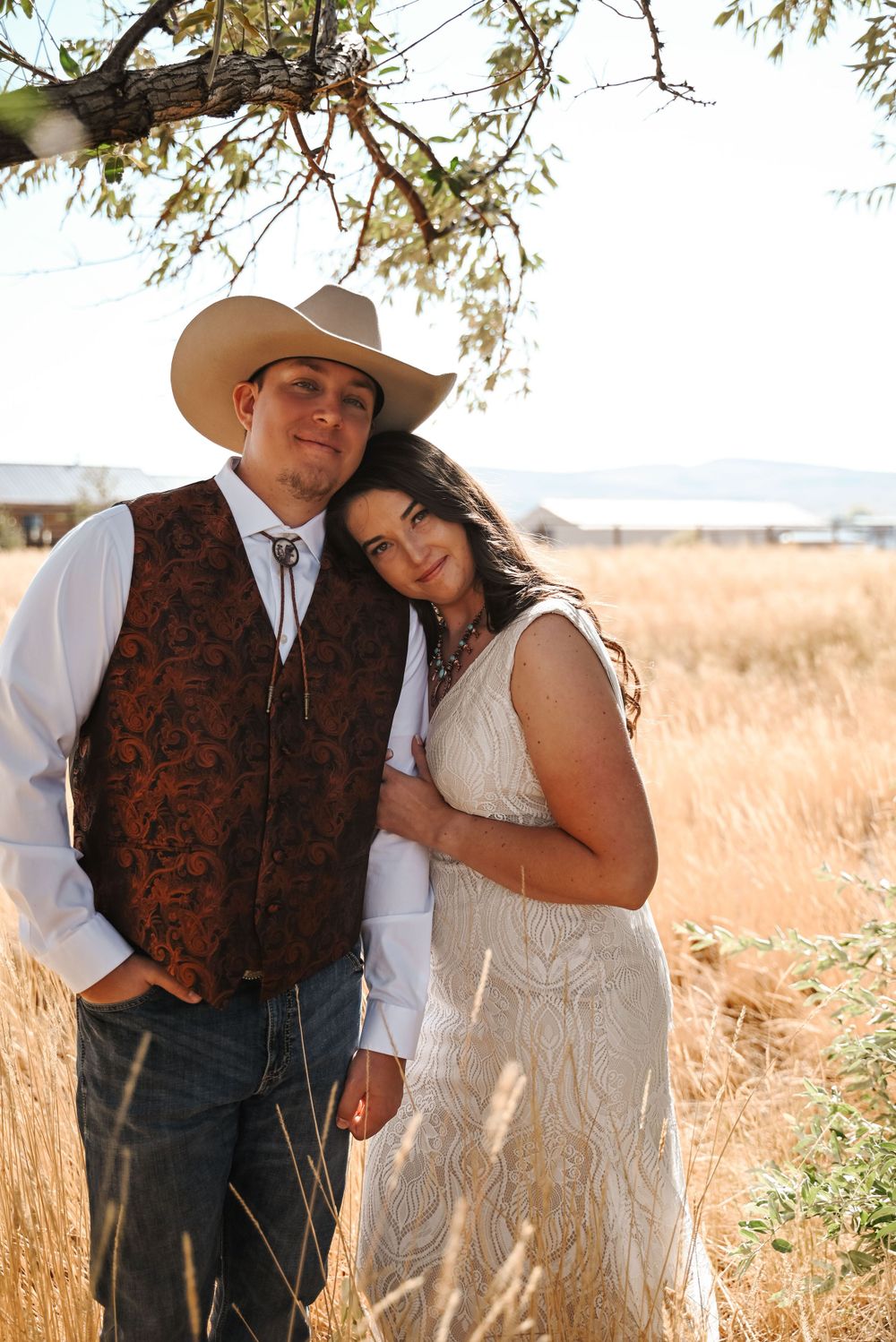 A western-themed couple poses together in a field during golden hour.