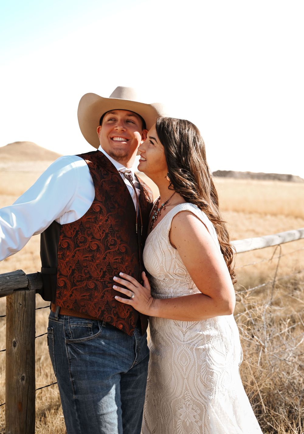 A romantic western-styled couple shares a tender moment by a rustic fence.