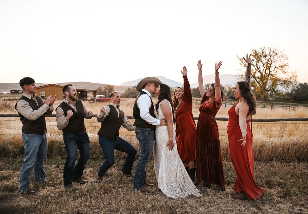 Wedding party in western attire and burgundy dresses posing playfully in a field at sunset.