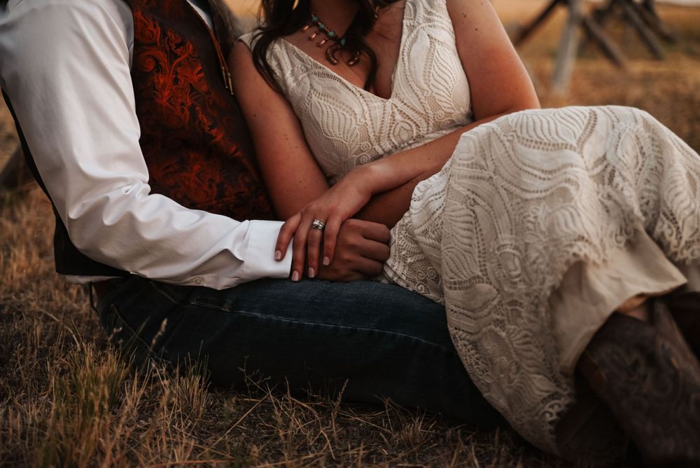 Close-up detail of couple's hands and wedding dress lace against rustic backdrop.