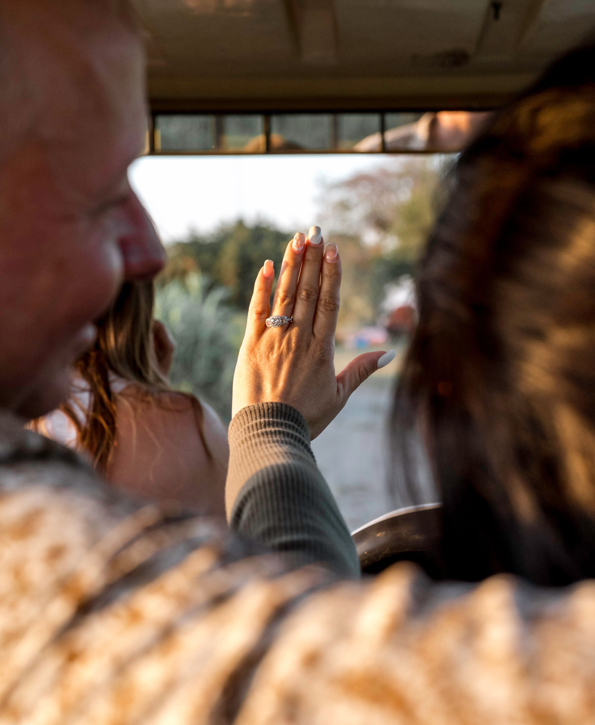 A hand held up to showcase a diamond engagement ring in natural sunlight.