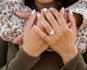 Close-up of hands clasped together showing off a sparkling engagement ring.