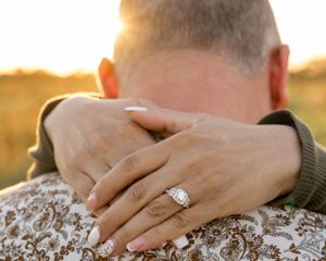 Hands embracing from behind while showcasing an engagement ring during golden hour.