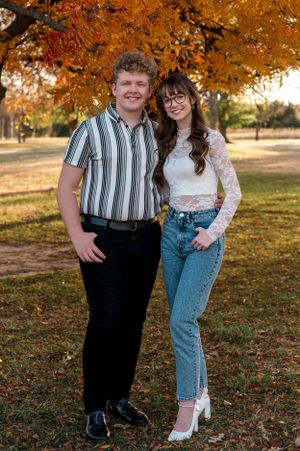 Retro-styled couple posing in autumn setting with orange fall foliage.