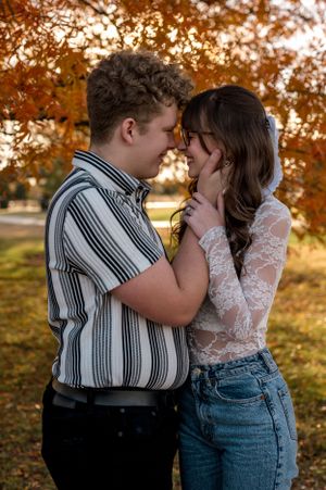 A romantic autumn portrait of a couple embracing outdoors with golden fall foliage in the background for engagement photoshoot.