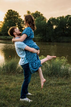 Two people share a romantic embrace while spinning in a grassy field at sunset.