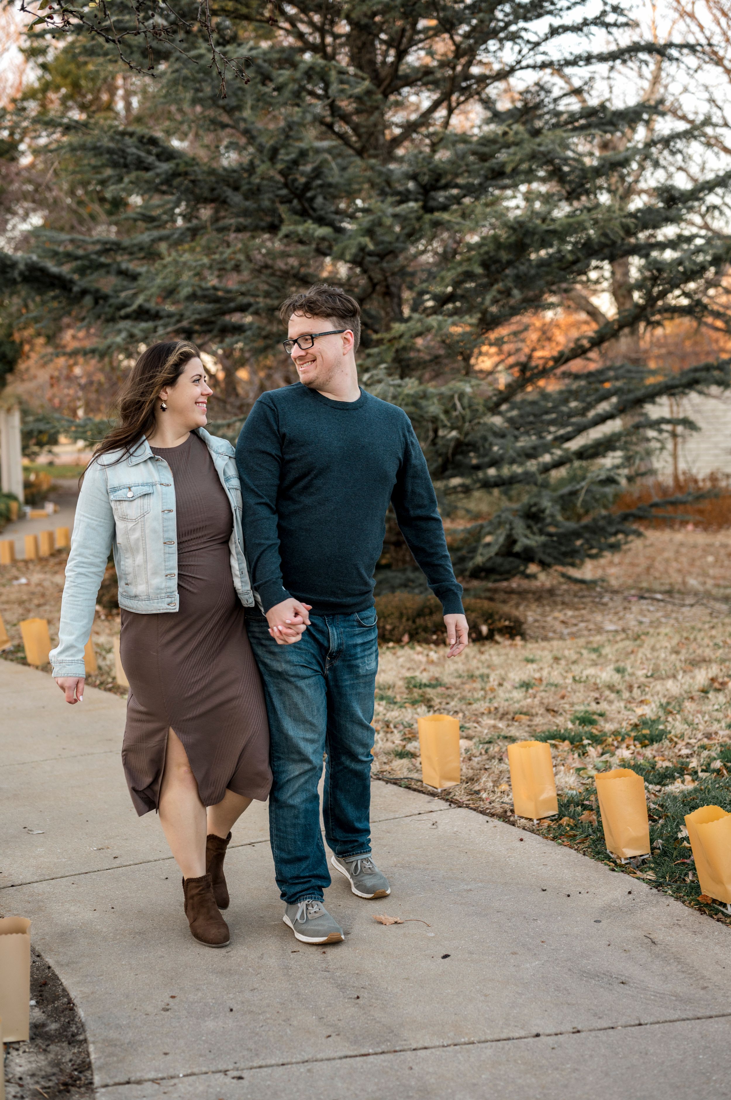 Couple strolling along path with luminaries and evergreen trees in autumn setting.
