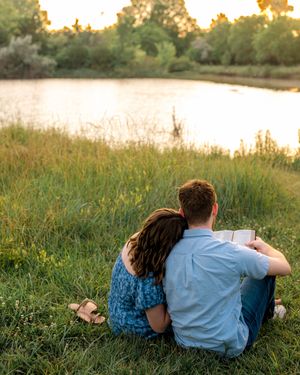 A couple relaxes together on grassy riverside bank during golden sunset hour.