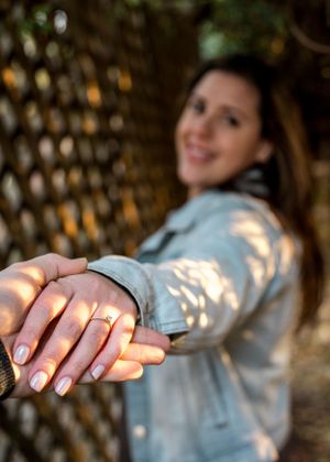 Close-up of hands showing engagement ring with dappled sunlight through lattice.
