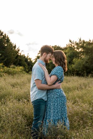 A romantic couple shares an intimate moment in a sunlit meadow during sunset.