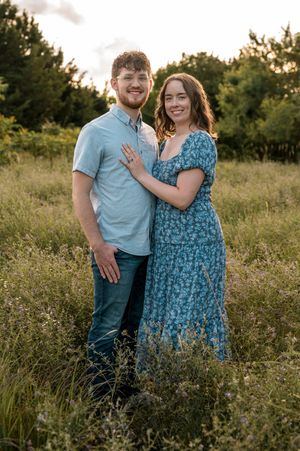 A couple in coordinating blue outfits embrace lovingly in a summer wildflower field during golden hour.