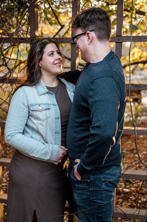 Couple in casual attire sharing intimate moment against autumn foliage backdrop.