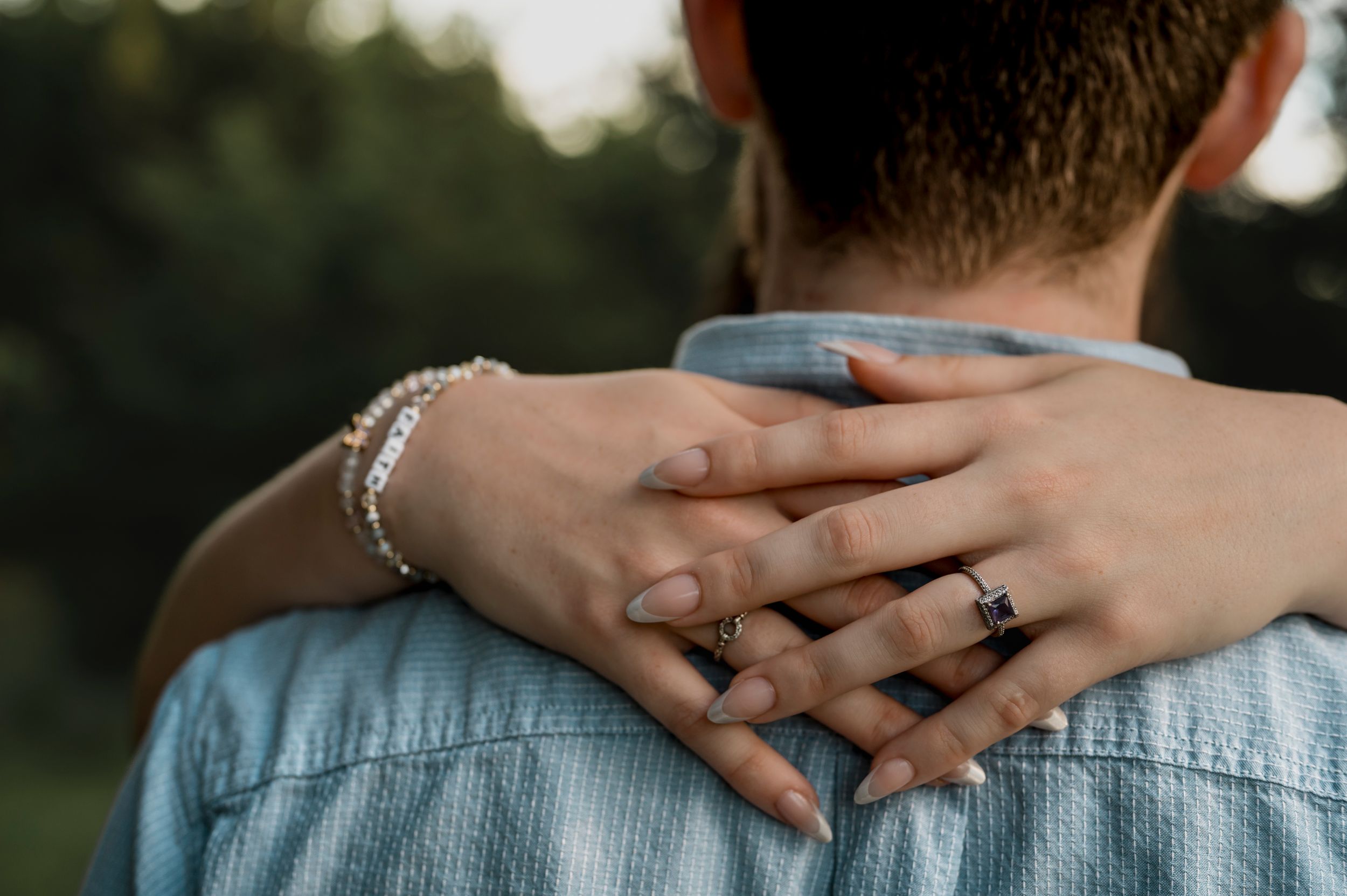 Close-up view of hands clasped around shoulders during an intimate outdoor photo session at dusk.