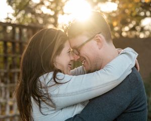 An intimate embrace captured at sunset with golden light streaming through a wooden fence.