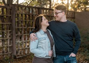 A couple shares a loving moment while standing near a wooden lattice fence during sunset.