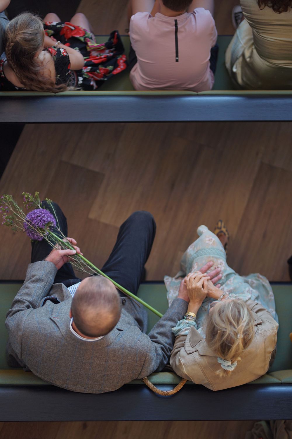 Overhead view of people resting on cushioned benches with purple flowers.