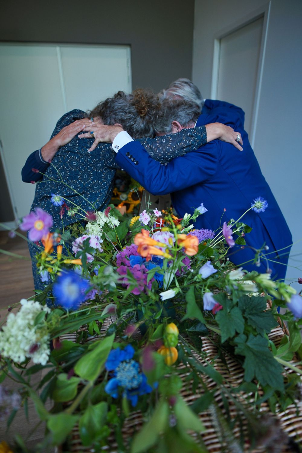 Multiple people embracing over a colorful floral arrangement.