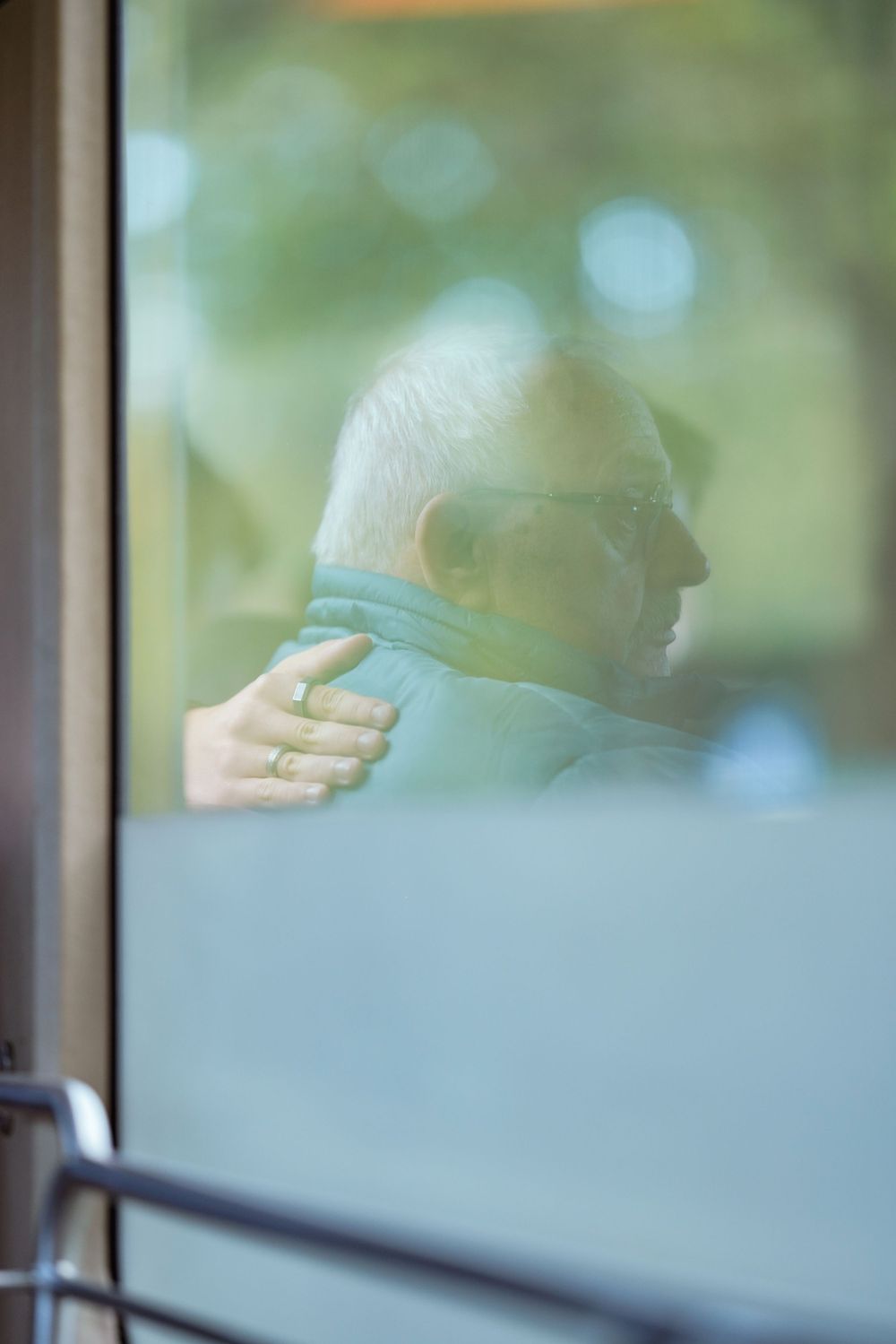 A hazy view through glass shows a person wearing blue in a soft-focus, dreamy composition with bokeh in the background.