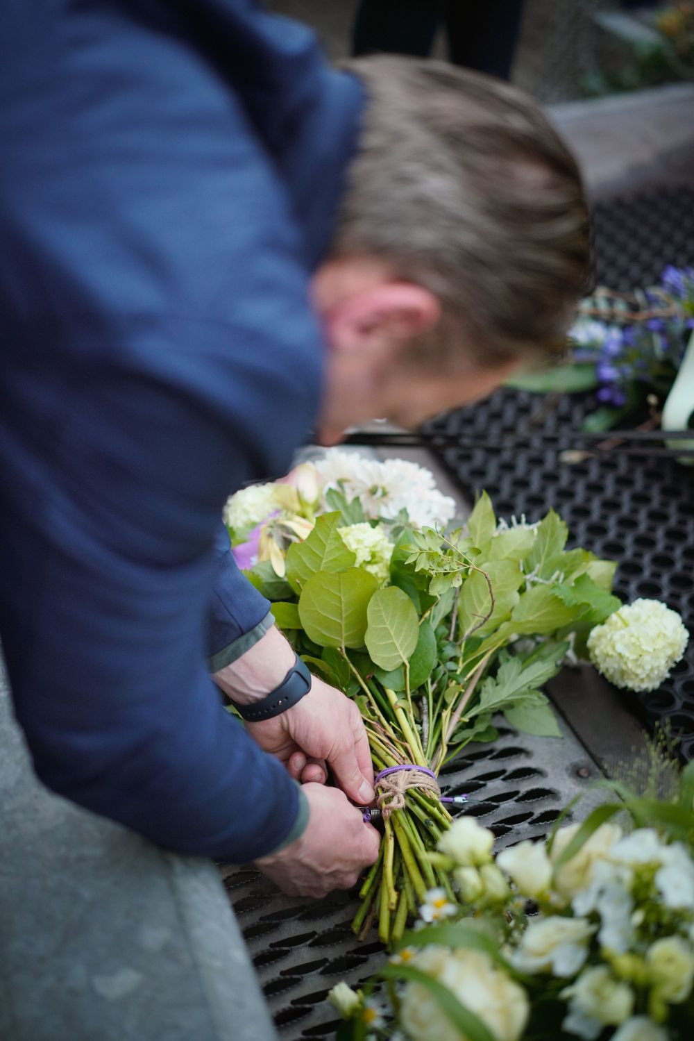 Florist arranging white hydrangeas and greenery into a fresh bouquet on an outdoor table.