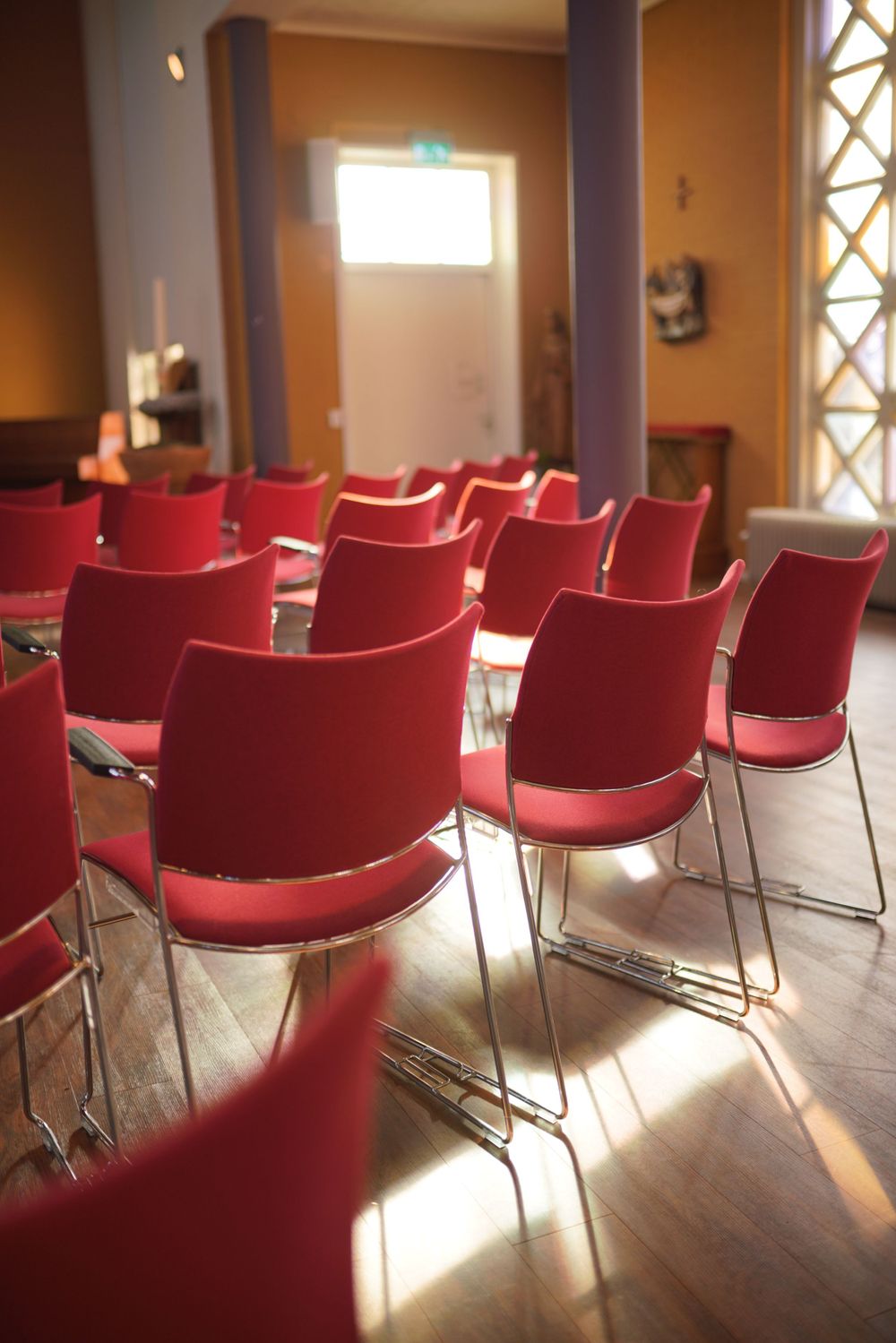 Empty red chairs arranged in rows in a sunlit room with warm walls.