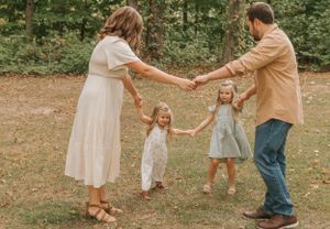Family members hold hands in a line while walking through a park setting.