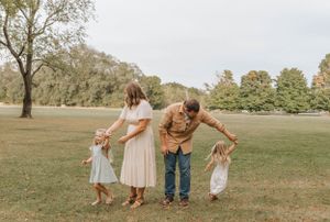 A family holds hands while walking together in a grassy park on a sunny autumn day.