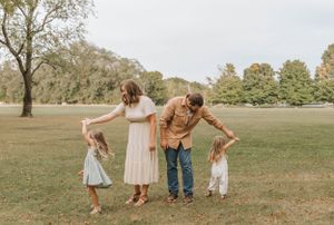A family shares a playful moment together while standing in a park setting.