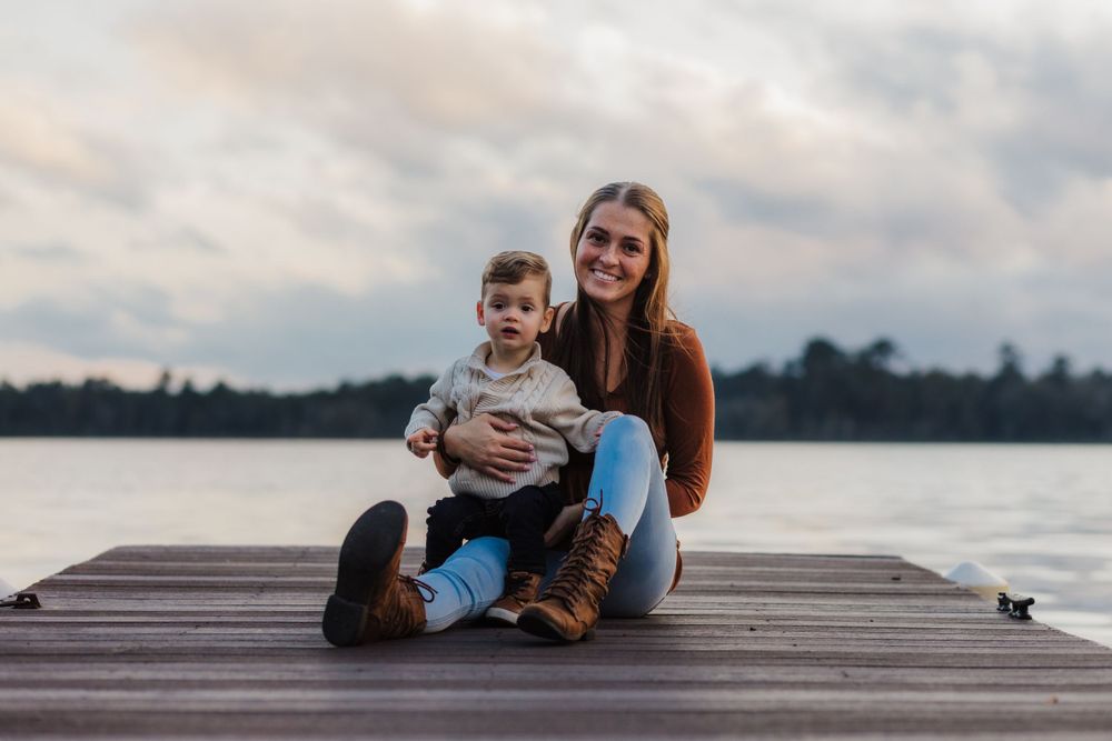 Serene lakeside portrait of parent and child sitting together on wooden dock at sunset.