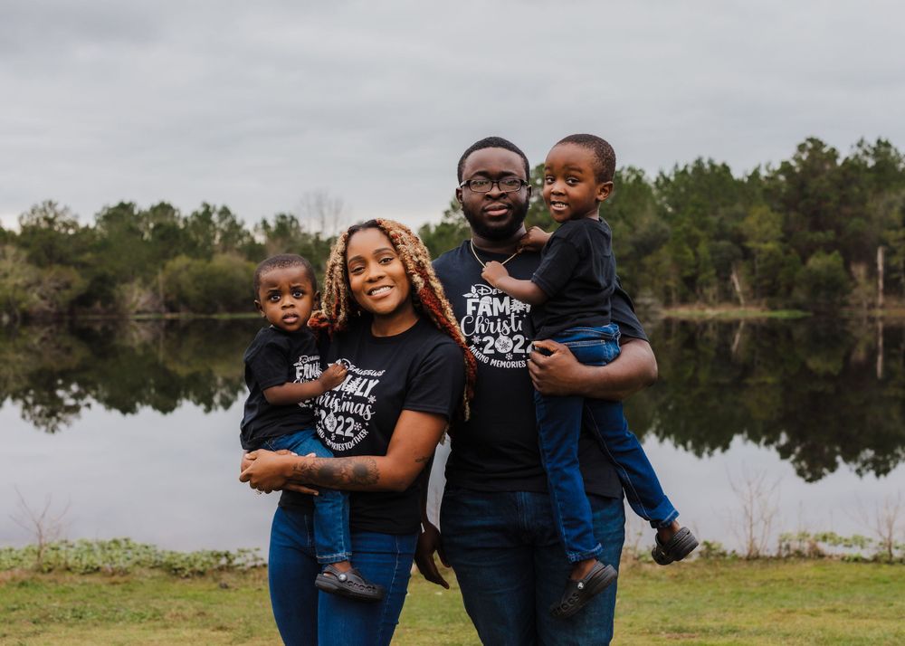 Family of four wearing matching t-shirts posing together by lake.