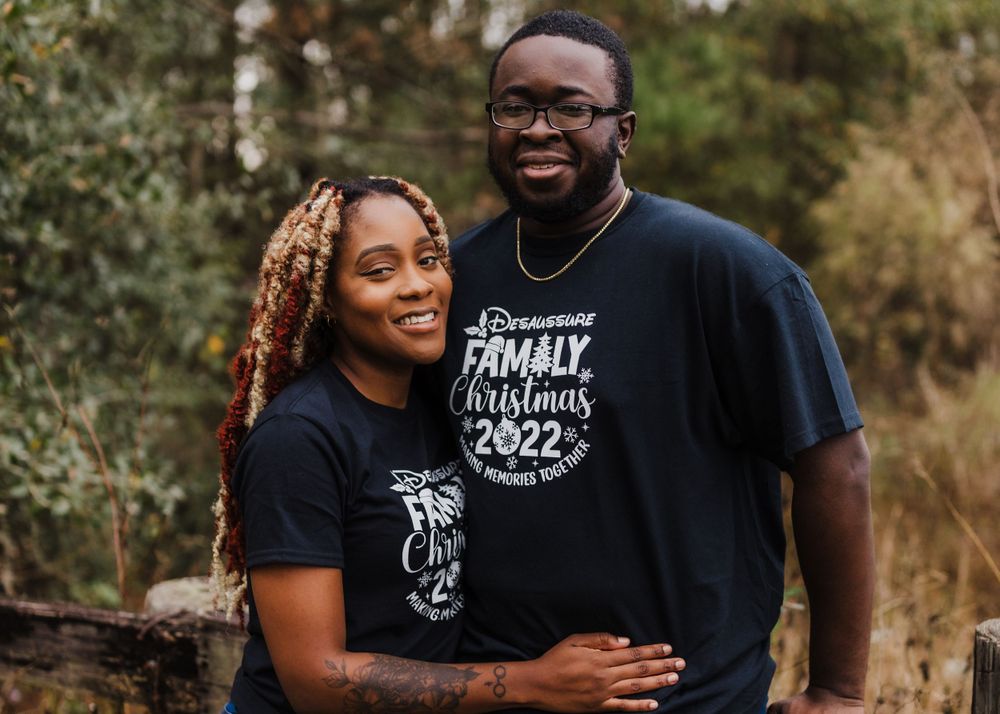 Couple wearing matching black t-shirts posing outdoors by lake.